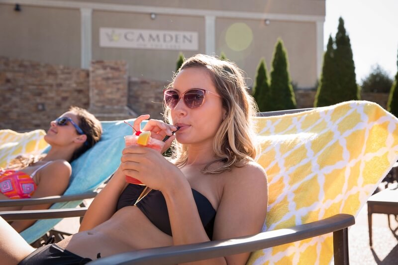 blonde woman drinking cocktail lounging by camden on the lake pool